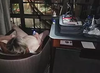 Hey, check out this granny getting naked and masturbating right in front of the city lights at night in a hotel.